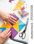 Small photo of female hands coordinates geometric color fabric pieces for patchwork quilt on a white background. the process of creating scrappy blankets. top view. flat lay.